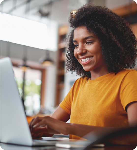 Image close up of your black woman working at a desk smiling and typing on a laptop.